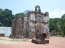 Stained ruin of a stone building, showing a central arch, flanked by two columns, with a stone relief above the arch, also flanked by two columns, and a second free-standing arch perched on the very top of the ruin.